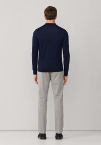 Granatowa, długiego rękawa, dzianinowa koszula polo z kołnierzykiem, połączona z jasnoszarymi spodniami i ciemnym obuwiem, widok z tyłu.