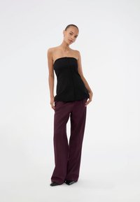 Black strapless top with front button details paired with wide-leg maroon trousers. The outfit features a smooth texture and relaxed fit.