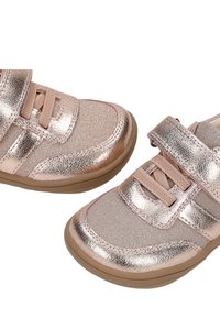 Paire de baskets brillantes couleur or rose pour tout-petits avec bandes Velcro, lacets en tissu et semelles en caoutchouc marron clair sur fond blanc.
