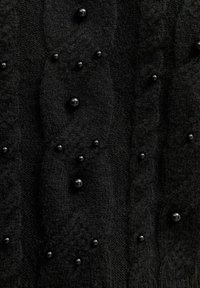 Maglione nero lavorato a maglia con un motivo a treccia e decorato con piccole perline nere distribuite uniformemente sul tessuto.