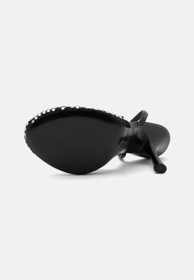 Chaussure noire à talon haut vue du côté de la semelle, présentant un bout pointu orné de petites perles brillantes et une fine bride au niveau du talon.