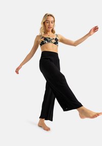 Pantaloni neri a gamba larga con un tessuto testurizzato e una vita elasticizzata, abbinati a un top corto a fiori nei toni del nero, rosa e verde.