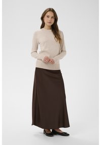 Bež pleten pulover z okroglim izrezom in rebrastimi manšetami, kombiniran z dolgo, gladko rjavo satenasto krilo. Obleko dopolnjujejo črni ploski čevlji.