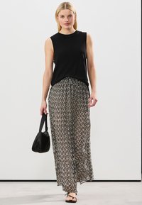 Haut noir sans manches associé à une longue jupe transparente à motifs noirs et beiges. Tient un petit sac à main noir. Sandales plates complètent le look.