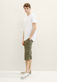 Weißes Rundhals-T-Shirt, olivgrüne Cargo-Shorts mit Seitentaschen und weiße Sneakers mit braunen Akzenten. Einfaches und funktionales Design.