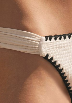Bikini bianco con tessuto testurizzato e accenti neri. Presenta una vita arricciata e dettagli di cucitura nera a contrasto.