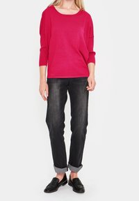 Fuchsia stickad tröja med rundad halsringning, lös passform och långa ärmar, kombinerad med mörka jeans med uppvikt midja och svarta loafers.