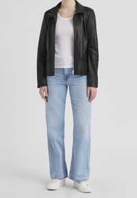 Černá kožená bunda s límcem a předním zipem, kombinovaná s světle modrými rozšířenými džíny a bílými teniskami, vše na neutrálním pozadí.