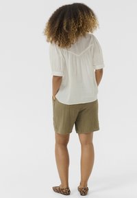 Blusa bianca a maniche corte con dettagli arricciati, abbinata a pantaloni corti testurizzati color verde oliva e ballerine con stampa leopardata.