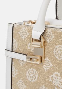 Beige patterned handbag with white leather accents, gold hardware, and a structured design featuring a prominent clasp detail.