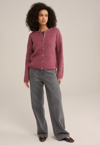 Vinske barve cardigan z teksturiranim pletenjem, ki ima okroglo ovratnico in zapiranje na gumb, v kombinaciji z sivimi širokima hlačami z visokim pasom.