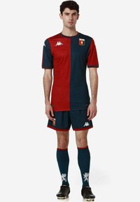 Futbalový dres s červeným a tmavomodrým tričkom, zodpovedajúcimi šortkami a ponožkami s grafiku leva; vyrobený z ľahkej a priedušnej látky.