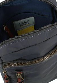 Interior de mochila negra de nailon con una correa amarilla, compartimento con cremallera y acento de cremallera metálica. Presenta detalles en cuero y etiqueta de logo.