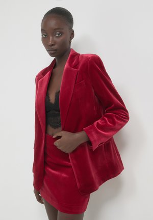 Red velvet blazer with oversized fit, notched lapels, and single chest pocket, paired with a matching velvet mini skirt. Lace bralette underneath.