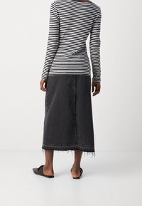 Gestreiftes Langarmoberteil in Schwarz und Weiß, kombiniert mit einem langen Jeansrock in Dunkelgrau, der einen ausgefransten Saum und schwarze Flip-Flops mit offenen Zehen hat.