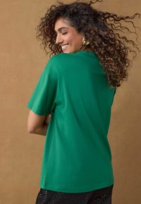 Groene katoenen t-shirt met een relaxed-fit en korte mouwen, voorzien van een ronde hals en zijnaad, gecombineerd met zwarte paillettenbroek.
