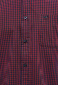 Camisa a cuadros rojos y azul marino hecha de tela ligera, con cierre de botones en la parte delantera, un bolsillo en el pecho y un pequeño logo bordado.