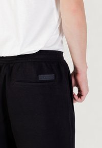 Zwarte sweatpants met een gladde textuur, voorzien van een achterzak en een donker etiket boven de zak, een elastische tailleband en zijnaad.