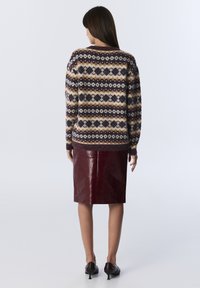 Woman wearing patterned knit sweater, burgundy leather pencil skirt, and black heeled shoes, standing against a plain background.