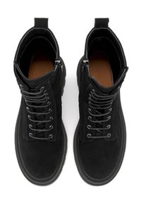 Botines de ante negro con cordones en la parte delantera, cremalleras en los laterales y suelas de goma texturizadas. Interior suave con una plantilla marrón.
