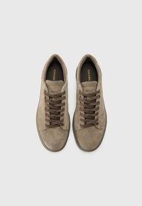 Baskets en suede beige avec des lacets marron, bout rond et semelles intérieures rembourrées. Le nom de la marque "GEOX" apparaît en doré sur la semelle intérieure.