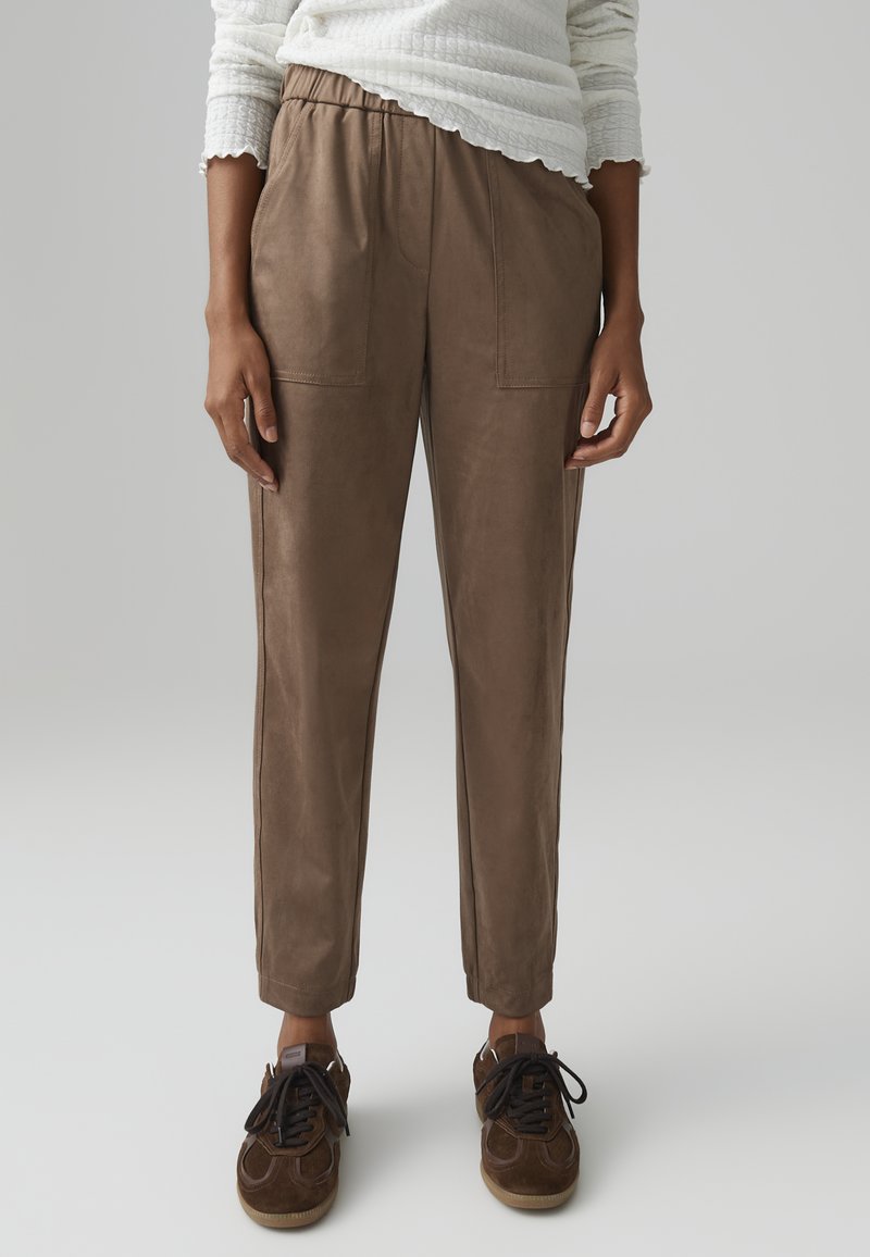 Brown faux leather pants with an elastic waistband, side pockets, and tapered legs, paired with dark sneakers. Smooth, textured finish.