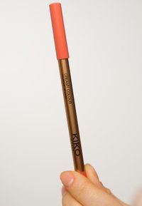 KIKO kremet leppestiftblyant i en bronsefarget beholder med oransje lokk, med svart skrift. Glatt tekstur, slank sylinderformet design.