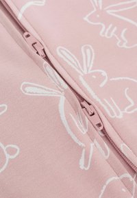 Rosa Stoffkleidung mit Reißverschluss, die weiße Hasenmuster aufweist. Der Reißverschluss ist in einer passenden rosafarbenen Nuance gehalten und hat eine strukturierte baumwollartige Oberfläche.
