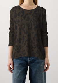 Top verde scuro con stampa leopardata nera, collo rotondo e maniche a tre quarti, abbinato a jeans in denim blu.