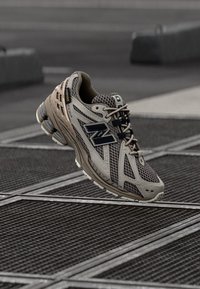 Beige och grå löparsko med övre del i mesh, böjd design, svarta detaljer, vadderad mellansula och texturerad yttersula för grepp.