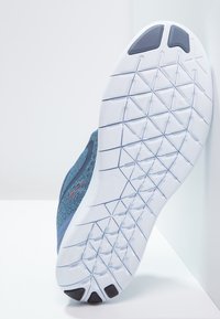 Modrá sportovní bota s texturovaným síťovaným svrškem a bílou gumovou podrážkou s geometrickým vzorem. Postranní akcenty v kontrastní barvě.