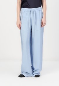 Pantalones de pierna ancha en azul claro con cinturilla elástica, cordón y dos bolsillos exteriores; textura suave y ajuste relajado.