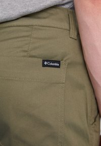 Olive zelene hlače z zadnjim žepom in črno oznako Columbia. Tkanina ima gladko teksturo in ojačane šive.