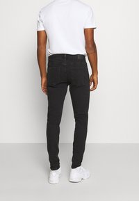Jeans ajustados negros de denim, con una cintura de altura media, bolsillos traseros y un corte slim. Combinados con una camiseta blanca lisa y zapatillas blancas.