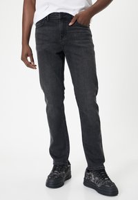 Jeans in denim grigio scuro con vestibilità dritta, design a cinque tasche e passanti per cintura, abbinati a sneakers texturate nere e grigie.