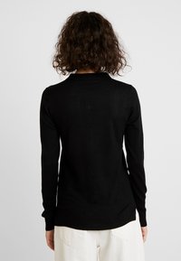 Zwarte trui met lange mouwen gemaakt van zachte stof, voorzien van een geribbelde zoom en manchetten, met een ronde hals en een aangesloten pasvorm.