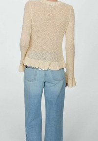 Sweter dzianinowy w jasnym beżu z długimi rękawami i falbaniastym dołem, w połączeniu z jasnoniebieskimi dżinsami o wysokim stanie, które prezentują luźny fason.