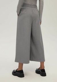 Szerokie spodnie w szarym materiale o gładkiej fakturze, z paskiem w talii i bocznymi kieszeniami, w połączeniu z czarnymi butami na platformie.