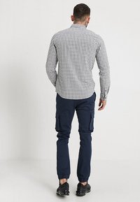 Camisa de cuadros en blanco y negro para hombre, combinada con pantalones cargo en color navy. La camisa cuenta con un cuello abotonado y mangas largas.
