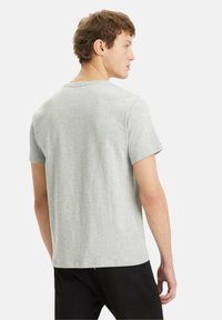 T-shirt grigio a maniche corte in cotone; presenta un collo rotondo e un orlo dritto; indossato con pantaloni neri. Texture liscia, design minimale.