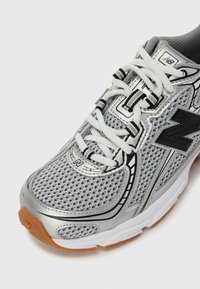 Grau sportif mit einem Obermaterial aus Netzstoff, weißen Schnürsenkeln, silbernen Akzenten und einer Sohle aus Gummi, konzipiert für Komfort und Atmungsaktivität.