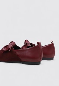 Zapatos planos burdeos hechos de cuero liso y ante, con un detalle de lazo en la parte delantera y un tacón bajo con punta redonda.