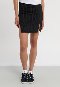 Svart miniskjørt med stripete mønster og sidespalter, laget av mykt stoff. Kombinert med svarte sneakers med hvite detaljer og logo.