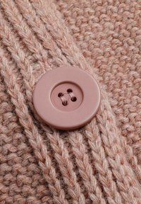 Getextureerd, zacht roze breiwerk met een ronde, lichtroze knop met twee kleine gaatjes, die de stof op zijn plaats houdt.