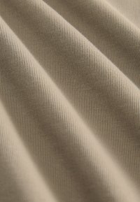 Beige ribbelstof met een gladde textuur, met zachte plooien en een consistent patroon van smalle lijnen.