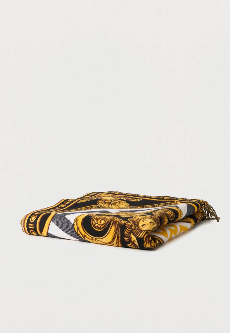 Διπλωμένο κασκόλ με μαύρα, χρυσά και λευκά περίτεχνα μπαρόκ μοτίβα και φούντες σε μία γωνία, εμφανιζόμενο σε λευκό φόντο.
