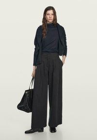 Pantaloni neri larghi abbinati a un dolcevita aderente blu navy e una giacca scura aperta. Una borsa tote nera texturizzata completa l'outfit.