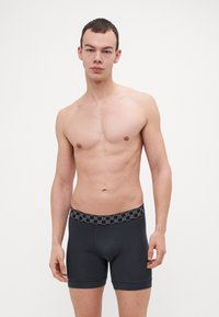 Boxeri negri cu un tiv texturat care prezintă un model repetitiv de logo, fabricați dintr-un material neted, elastic.