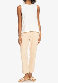 Witte mouwloze top met subtiele textuur, gecombineerd met beige rechte broek. Gekozen met tan gevlochten slide sandalen.