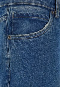 Denim jeans with a medium blue wash, featuring a back pocket, contrast stitching, and a small metal rivet accent on the pocket.